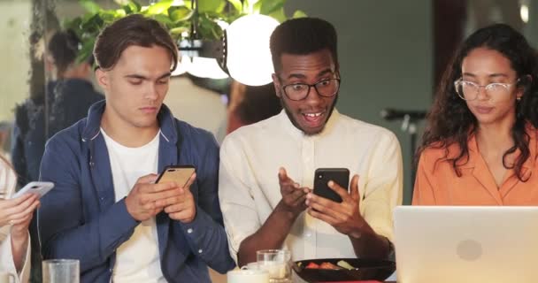 Millennial afro Αμερικανός τύπος δείχνει το περιεχόμενο smartphone στους συναδέλφους και χαρά. Χαρούμενοι νέοι startupers που αναζητούν ιδέες ενώ χρησιμοποιούν gadgets. Έννοια της επιτυχίας και της ομαδικής εργασίας. — Αρχείο Βίντεο