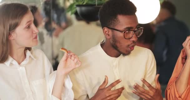 Vista de cerca del chico afroamericano compartiendo idea con sus colegas mientras comen en la cafetería. Jóvenes comunicándose durante el almuerzo. Concepto de comer fuera y amistad . — Vídeos de Stock