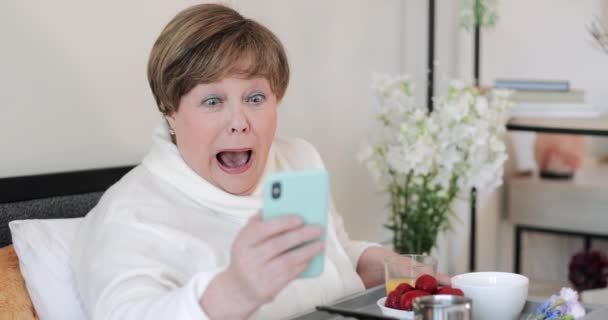 Close up of elderly woman having good news and cant believe her eyes while using smartphone. Old retired lady making surprised face while having breakfast and looking at phone screen. — Stock Video