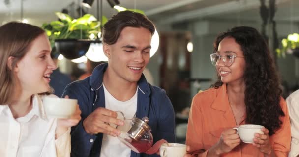 Milenyum meslektaşları rahat bir kafede otururken yemek yiyip sohbet ediyorlar. Genç yakışıklı adam arkadaşlarıyla sohbet ederken fincanına çay dolduruyor. İletişim kavramı. — Stok video