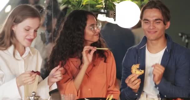 Crop view de jeunes gens joyeux riant et bavardant tout en passant du temps ensemble. Des amis millénaires souriants mangeant de la nourriture et parlant assis à table dans un restaurant confortable. — Video