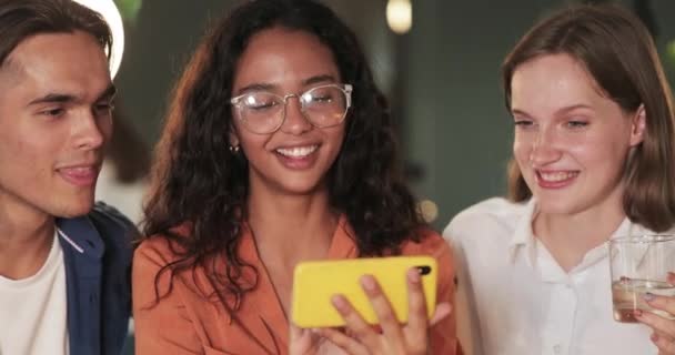 Detailní záběr mladé ženy držící telefon v horizontálním režimu krajiny při zobrazování přátel legrační fotografie. Tisíciletí lidé se smějí a dívají se na obrazovku mobilního telefonu. Indoors. — Stock video