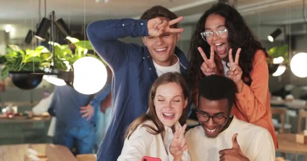 Pessoas alegres rindo e agindo como um tolo enquanto olham para a tela do smartphone. Amigos felizes tirando selfies enquanto passam tempo juntos em um restaurante acolhedor. Conceito de emoções positivas . — Vídeo de Stock