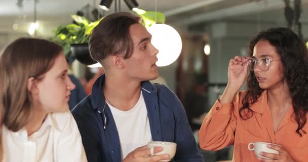 Crop view of young colleagues drinking coffee and talking while having break. Des gens du millénaire qui réussissent à avoir une conversation et à partager des idées tout en étant assis à table. À l'intérieur. — Video