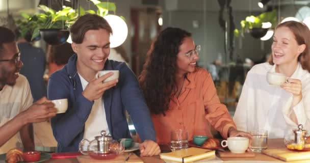 Glada tusenåriga vänner dricka te och skratta medan du sitter i mysiga café. Glada ungdomar som pratar och visar positiva känslor samtidigt som de har roligt tillsammans. — Stockvideo