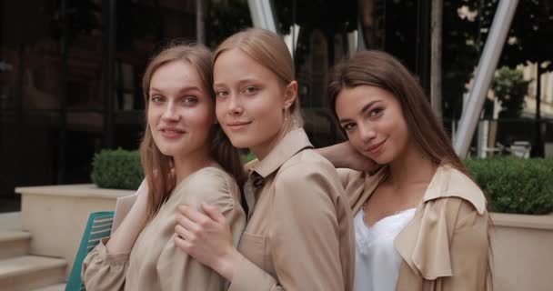 Zblízka pohled na tři atraktivní dívky dívá na kameru a usmívá se. Portrét stylových přítelkyň s nákupními taškami pózujících na městské ulici. Pojem přátelství. — Stock video