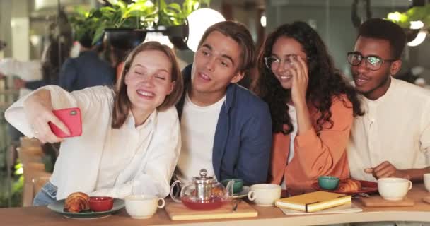 Les jeunes rient et saluent tout en ayant un appel vidéo dans un restaurant confortable. Fille heureuse tenant smartphone horizontalement tout en regardant avec des amis à l'écran. Concept d'émotions positives. — Video