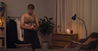 Yakışıklı sakallı adam akıllı telefonundan iyi haberler alıyor ve seviniyor. Banyo havlusundaki mutlu adam mesaj alıyor ve evde dans etmeye başlıyor. Başarı kavramı ve mutlu insanlar.