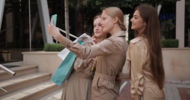 Kadın arkadaşlar alışveriş torbalarıyla selfie çekiyorlar. Şehir caddesinde duruyorlar. Çekici kadınlar telefonda konuşurken poz verip gülüyorlar ve ekrana bakıyorlar. Arkadaşlık kavramı.