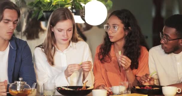 Young happy guys and girls communicating while eating and drinking in cosy restaurant. Millennial people talking and enjoying leisure time. Concept of friendship and happiness. — Stock Video