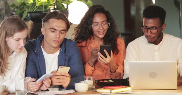 Χαρούμενη κοπέλα που δείχνει το περιεχόμενο του smartphone της σε συναδέλφους και χαίρεται στο cafe. Νέοι που αναζητούν λύση ενώ χρησιμοποιούν gadgets. Έννοια της επιτυχίας και της ομαδικής εργασίας. — Αρχείο Βίντεο