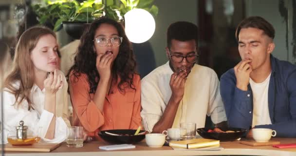 Мультирасовая группа друзей наслаждается вкусной едой, сидя в современном кафе. Тысячелетние эмоциональные люди едят пищу, проводя время вместе после работы. Концепция питания вне дома. — стоковое видео