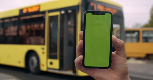Στενή άποψη του ανδρικού χεριού που κρατά mocked up οθόνη κινητό τηλέφωνο στο δρόμο. Έννοια του χρωματικού κλειδιού, πράσινη οθόνη και τεχνολογία. Θολή σύγχρονο λεωφορείο στέκεται στο παρασκήνιο. — Αρχείο Βίντεο