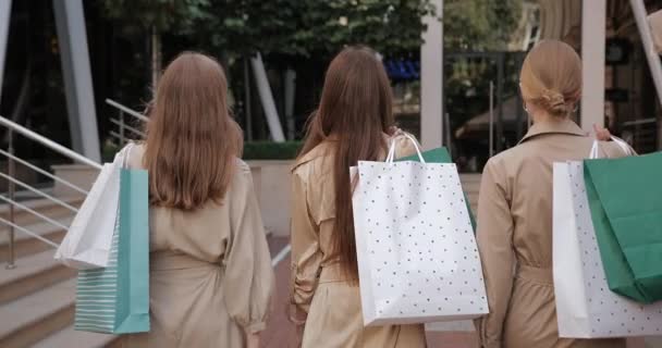 Widok z tyłu stylowe millenium dziewcząt w modne ubrania niosące torby papierowe po zakupach. Tysiącletnie przyjaciółki spacerujące ulicą. Pojęcie czasu wolnego i stylu życia. — Wideo stockowe