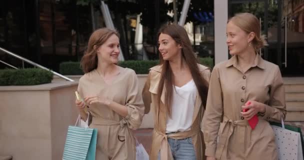 Jeunes filles attrayantes embrassant ensemble et souriant tout en tenant des sacs en papier. Femmes attrayantes riant tout en marchant dans la rue de la ville après avoir fait du shopping. Concept d'amitié. — Video