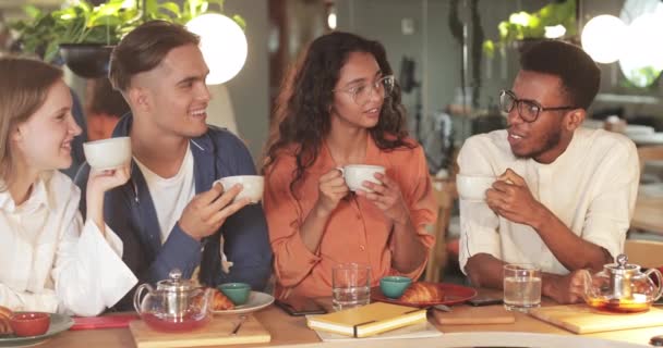 Afslappede kolleger, der holder kopper og smiler, mens de sidder i hyggelig restaurant. Glade unge mennesker chatter og viser positive følelser, mens de har det godt sammen. – Stock-video