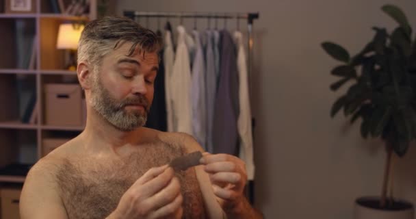 Close up view of puzzled man in 40s applying nose strip mask and looking in mirror.Funny bearded bachelor doing beauty procedure at his apartment in evening. — Stock Video