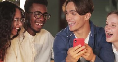 Mobilephone ekranına bakıp gülen neşeli arkadaşların ekili görüntüsü. Bir grup gülümseyen insan komik fotoğraflara bakıyor. Arkadaşlık kavramı ve olumlu duygular. Kapalı.