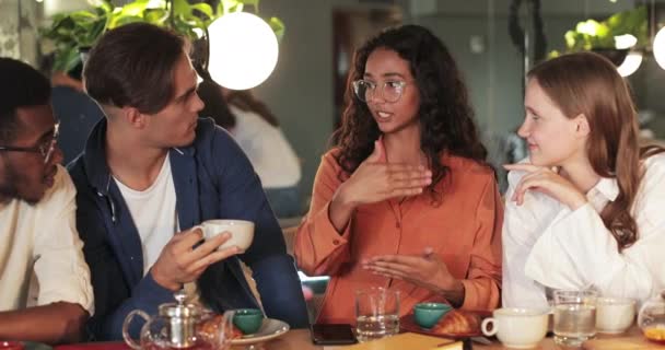 Good looking girl in glasses gesturing while telling funny story her friends in cosy cafe. Cheerful young colleagues listening woman and laughing while having lunch.Concept lifestyle. — Stock Video