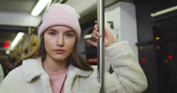 Porträtt av ung söt flicka tittar på kameran medan du går på kollektivtrafik. Närbild bild av attraktiv tusenårig kvinna i rosa hatt poserar samtidigt pendling hem på kvällen. — Stockvideo