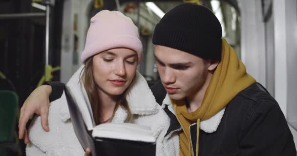 Joven pareja leyendo libro juntos mientras están sentados en el autobús. Un chico encantador abrazando a su novia mientras disfrutan de la historia y van en transporte público por la noche. Concepto de estilo de vida . — Vídeos de Stock