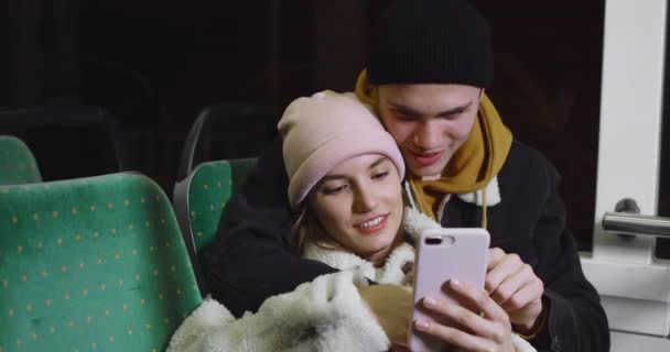 Beautiful girl scrolling smartphone while leaning on her handsome boyfriend. Cheerful young couple looking at phone screen while going at public transport. Concept of relationship. — Stock Video