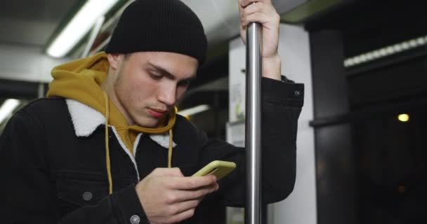 Vue rapprochée du gars millénaire en utilisant son smartphone tout en allant dans les transports en commun. Beau jeune homme défilant flux d'informations dans les médias sociaux et tapant sur l'écran. Concept de technologie. — Video