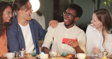 Afro-Amerikalı genç adam arkadaşlarına komik videolar gösterirken telefonu yatay manzara modunda tutuyor. Gençler kahkahalarla gülüyor ve kafede vakit geçirirken cep telefonu ekranına bakıyor.