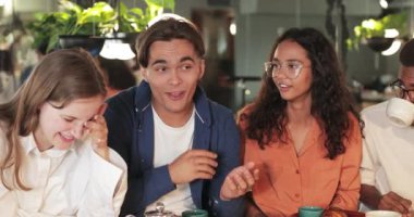 Hoş bir restoranda çok ırklı iş arkadaşlarıyla otururken komik hikâyeler anlatan yakışıklı bir adam. Dinlerken gülen neşeli gençler. Olumlu duygular kavramı.