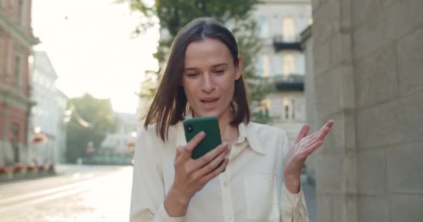 Närbild av ung kvinna säger wow och leende medan du tittar på telefonskärmen. Glada flicka att göra förvånad ansiktsuttryck när du använder smartphone och promenader på stadens gata. — Stockvideo