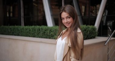 Esmer saçlı, poz veren ve kameraya bakan çekici bir genç kadın portresi. Milenyum kadınlarının şık kıyafetler giyip şehir caddesinde dikilirken çekilmiş görüntüsü. Duyguların kavramı.