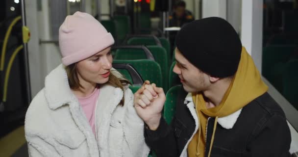 Jóvenes alegres sosteniendo sus manos y hablando mientras van en tranvía por la noche. Millennial pareja coqueteando y sonriendo mientras se divierten juntos. Concepto de la vida real. — Vídeo de stock