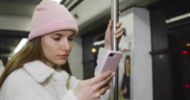 Vista de perto da jovem mulher usando seu smartphone enquanto vai no transporte público. Mulher jovem atraente rolando feed de notícias nas mídias sociais e tocando na tela. Conceito de tecnologia. — Vídeo de Stock