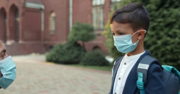 Άποψη των καλλιεργειών του νεαρού πατέρα και ο γιος του φορώντας ιατρικές προστατευτικές μάσκες αγκαλιάζει στην αυλή. Ο μπαμπάς και το παιδί του με σακίδιο να λένε αντίο την πρώτη μέρα στο σχολείο. Έννοια του ιού, εκπαίδευση. — Αρχείο Βίντεο