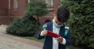 Tıbbi koruyucu maskeli bir çocuk sokakta yürürken akıllı telefonuyla oyun oynuyor. Okul yolunda üniformalı bir çocuk telefon ekranını dinliyormuş. Oyun kavramı .