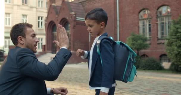 Jonge vader in pak en tienerjongen die afscheid neemt voordat hij naar school gaat. Kind in uniform en met rugzak punch man hand en geven high five voor het lopen op lessen. — Stockvideo