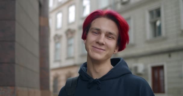 Portrét mladého hipsterského muže s rudě obarvenými vlasy, hledícího do kamery. Zblízka pohled na tisíciletého chlapa v tmavé mikině usmívajícího se na ulici. Pojem lidské emoce. — Stock video