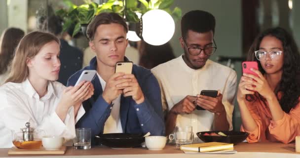 Vista Crop di amici millenari phubbing smartphone mentre trascorrono del tempo insieme in caffè. Gruppo di giovani che scorrono i notiziari sui social network mentre siedono a tavola. — Video Stock