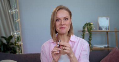 Kameraya ruj sunan ve evdeki kanepede otururken konuşan neşeli bayan vloger. Gülümseyen kadın kozmetik ürün incelemesini kaydediyor. Vlog yazma ve güzellik kavramı.