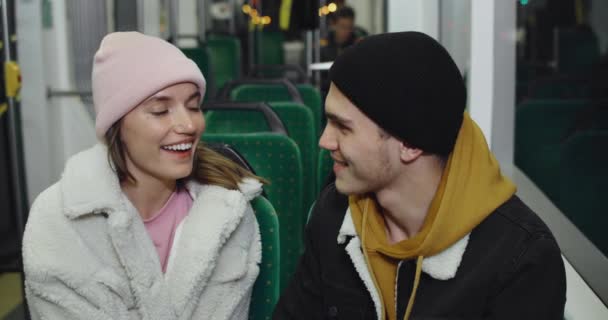 Schöne Millennial-Paar kommunizieren und lächeln, während sie in der Straßenbahn sitzen. Fröhliche Kerle und Mädchen, die sich unterhalten, während sie nach dem Date in öffentlichen Verkehrsmitteln nach Hause fahren. Konzept des realen Lebens. — Stockvideo