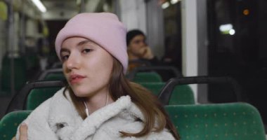 Toplu taşıma aracıyla giderken müzik dinleyen kulaklıklı güzel bir genç kadının portresi. Gece tramvayda oturan kızın yakın görüntüsü. İnsan ve yaşam tarzı kavramı.