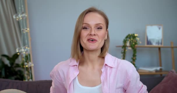 Kobieta influencer macha cześć i pokazuje kciuk do góry podczas nagrywania wideo do jej vlog piękna. Wesoła dziewczyna mówi i uśmiecha się patrząc do kamery i siedzi na kanapie. — Wideo stockowe