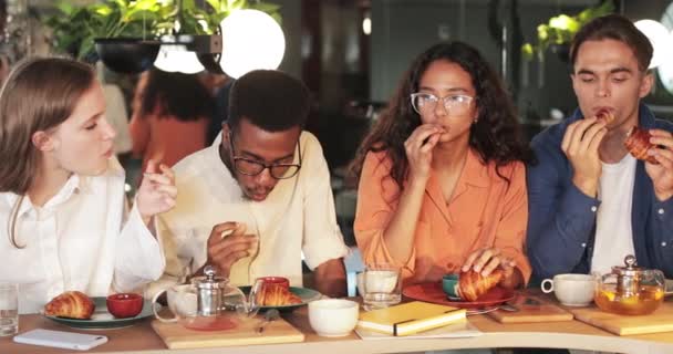 Amis milléniaux savourant de délicieux croissants tout en étant assis dans un café moderne. Groupe de jeunes mangeant tout en passant du bon temps ensemble après le travail. Concept de manger dehors. — Video
