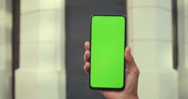 Akıllı telefonu tutan ve yeşil boş ekrana basan kadının yakın görüntüsü. Model ve krom anahtar kavramı. Arkaplanda kapalı bina.