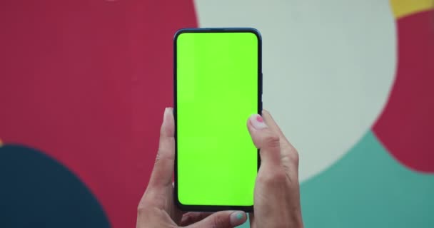 スマートフォンを持ち、モックアップ画面を押して流行の爪のデザインと女性の手のビューを閉じます。緑の画面とクロマキーの概念。カラフルなスポット背景. — ストック動画