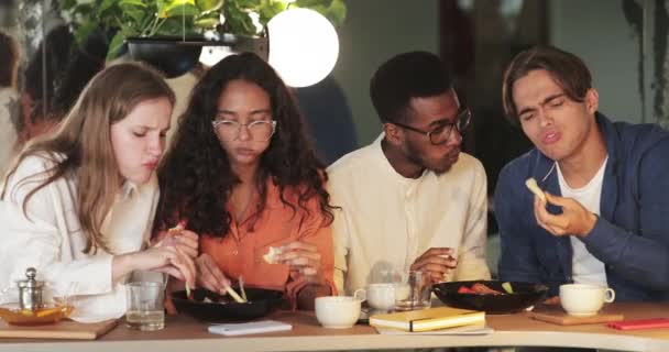 Crop view of young hungry friends eating tasty food in cafe during meeting. Étudiants pluriethniques millénaires savourant et partageant un repas tout en étant assis à une table de restaurant confortable. — Video