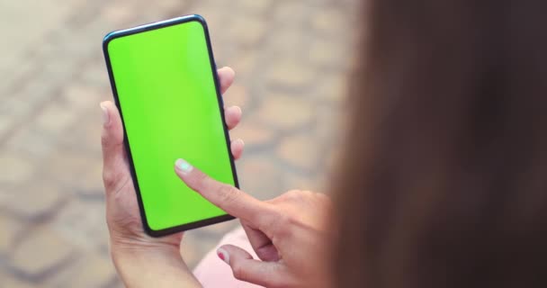 Sopra vista di spalla di persona femminile che tiene e preme su smartphone con schermo di mockup mentre si siede a strada. Concetto di chiave cromatica e schermo verde. — Video Stock