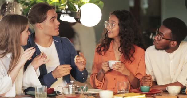 Young handsome guy telling funny story to friends while they having good time in cafe. Millennial friends eating and drinking while communicating during lunch. Concept of eating out. — Stock Video