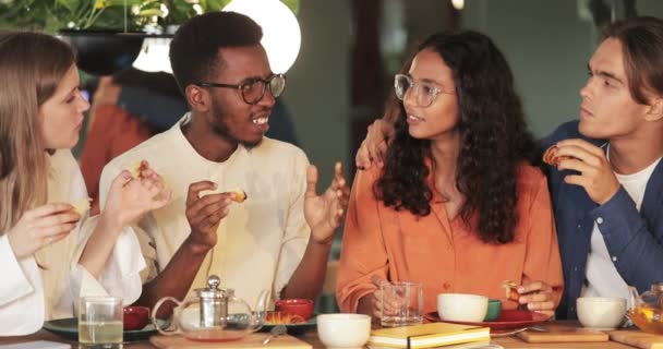 Pemuda Afrika Amerika menceritakan kisah kepada teman-teman sementara mereka menghabiskan waktu yang baik di kafe. Teman yang ceria makan dan berkomunikasi saat makan siang. Konsep makan di luar dan persahabatan. — Stok Video