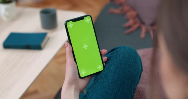 Vista trasera de la mujer sosteniendo y mirando la pantalla de la maqueta del teléfono inteligente. Persona femenina usando el teléfono mientras está sentada en el sofá en casa. Concepto de croma key y pantalla verde. — Vídeo de stock